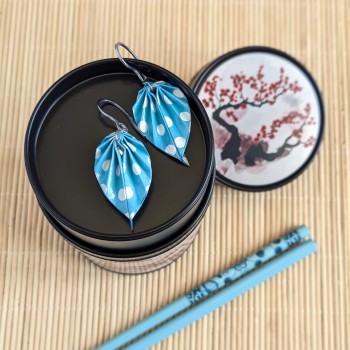Boucles d’oreilles feuilles en origami à pois blancs sur fond bleu ciel, dans une mise en scène inspirée de l’univers japonais.